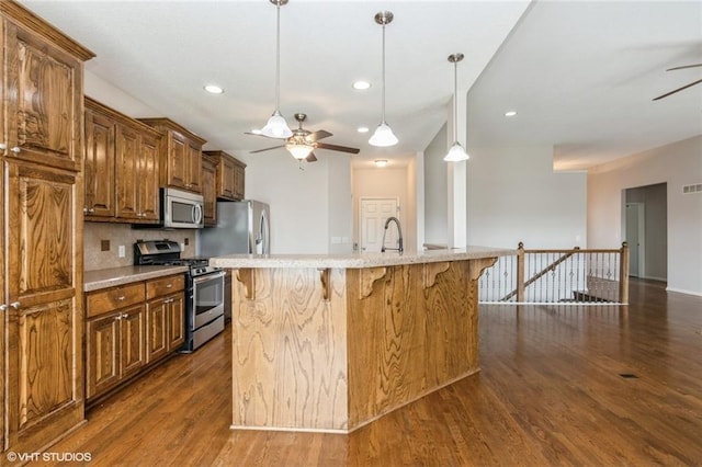 kitchen with a ceiling fan, dark wood-style flooring, appliances with stainless steel finishes, pendant lighting, and a kitchen bar