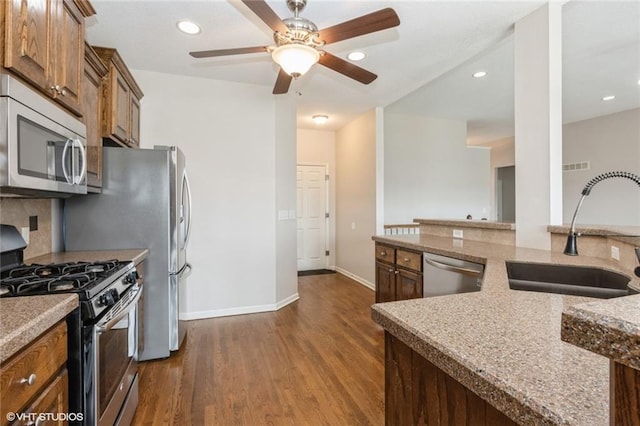 kitchen featuring a ceiling fan, a sink, stone countertops, dark wood finished floors, and appliances with stainless steel finishes