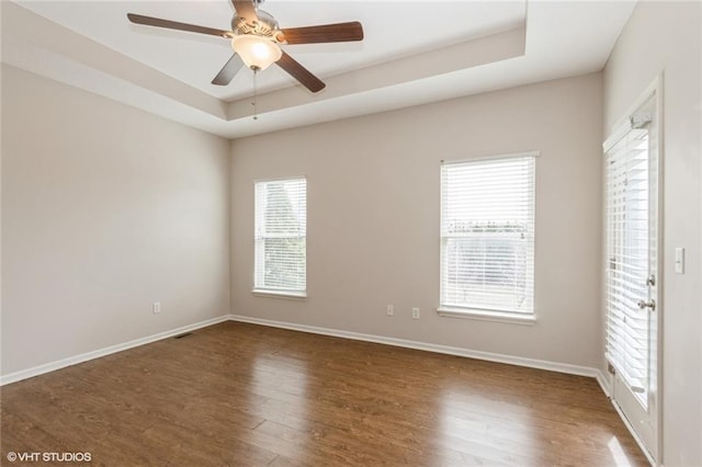 unfurnished room featuring baseboards, a ceiling fan, a tray ceiling, and wood finished floors