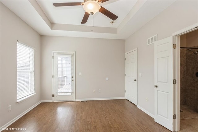 spare room featuring a ceiling fan, wood finished floors, visible vents, baseboards, and a tray ceiling