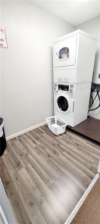 washroom featuring laundry area, stacked washing maching and dryer, wood finished floors, and baseboards