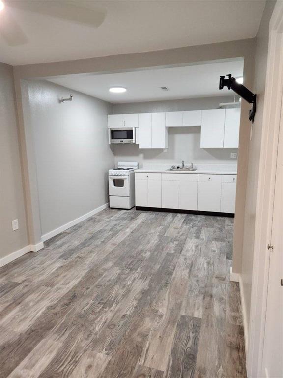 kitchen featuring gas range gas stove, a sink, white cabinets, light wood finished floors, and stainless steel microwave