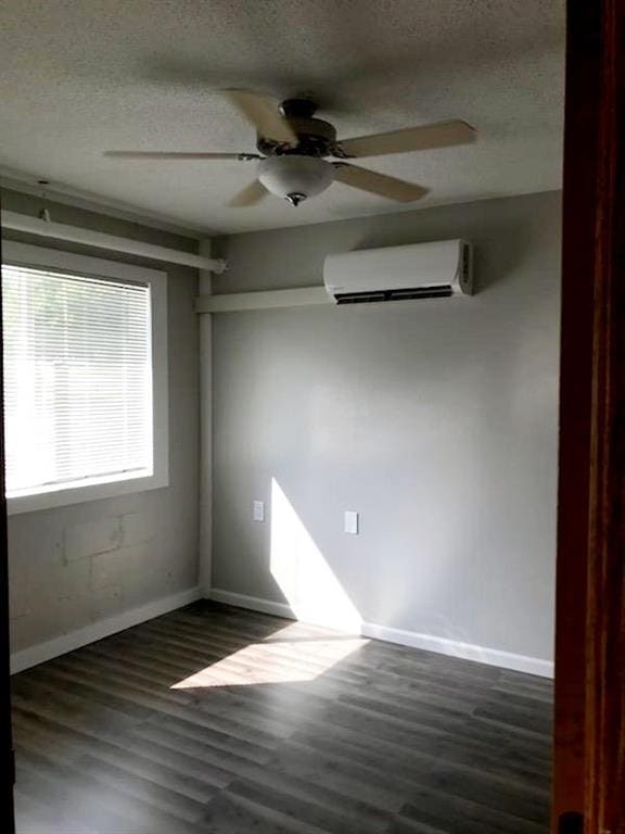 empty room with dark wood-type flooring, a wall mounted air conditioner, a textured ceiling, and baseboards