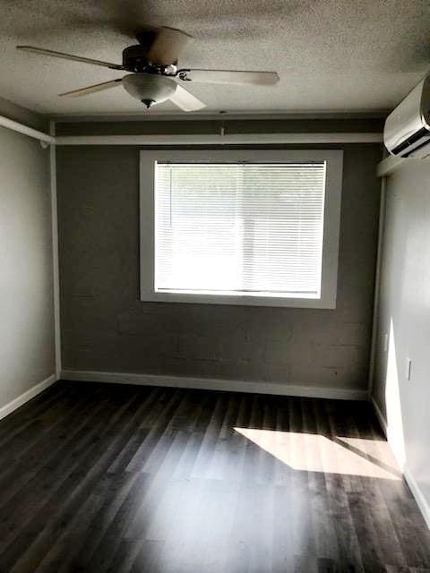 unfurnished room featuring a textured ceiling, ceiling fan, baseboards, an AC wall unit, and dark wood finished floors
