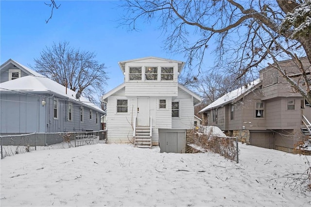 snow covered back of property with entry steps, a garage, and fence