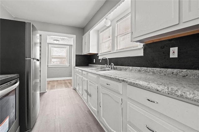 kitchen with decorative backsplash, stainless steel range with electric cooktop, light wood-style floors, white cabinets, and a sink