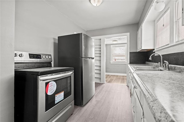 kitchen featuring a sink, stainless steel appliances, light countertops, light wood-style floors, and white cabinetry