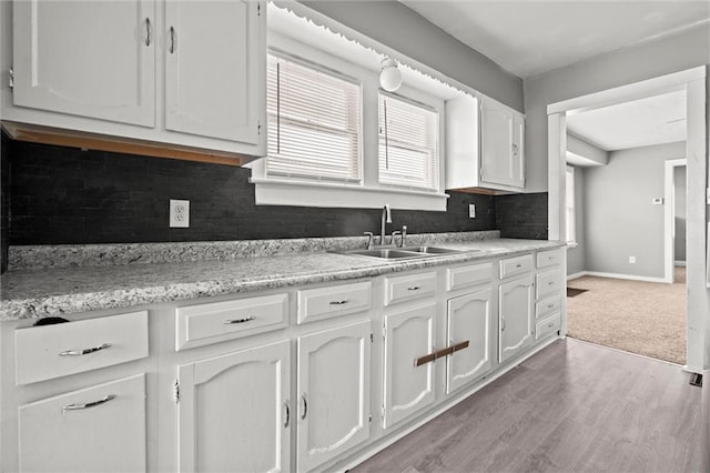 kitchen with baseboards, a sink, light countertops, white cabinetry, and tasteful backsplash