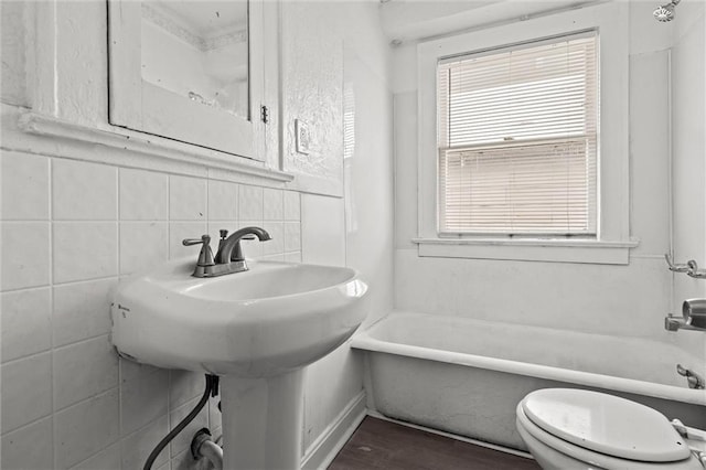 full bath featuring tile walls, toilet, and a tub