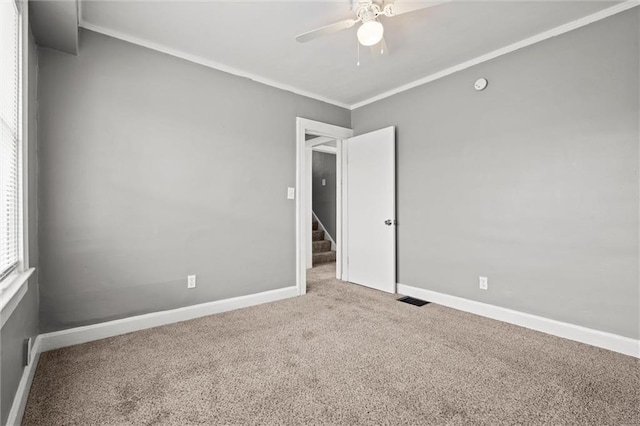 carpeted empty room with visible vents, baseboards, ornamental molding, and a ceiling fan