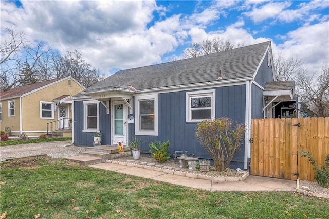 bungalow with a shingled roof, a gate, fence, and a front yard