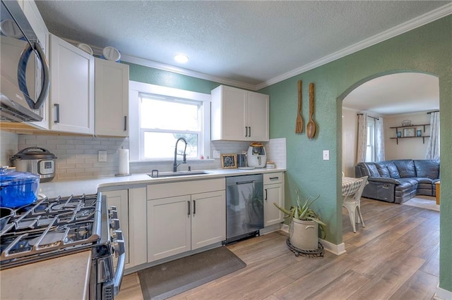 kitchen with arched walkways, a sink, appliances with stainless steel finishes, light wood-type flooring, and crown molding