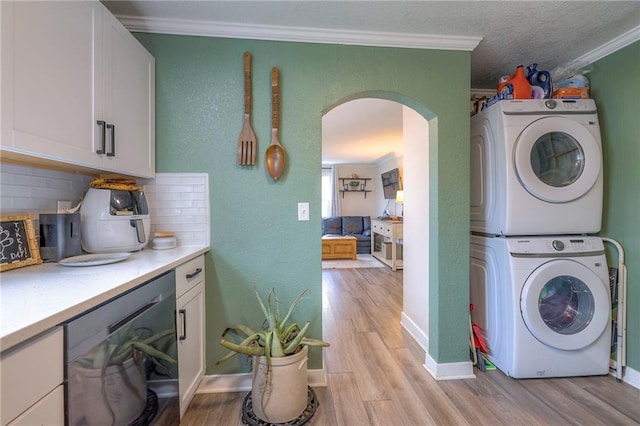 laundry area featuring arched walkways, stacked washer and clothes dryer, crown molding, light wood-style floors, and laundry area