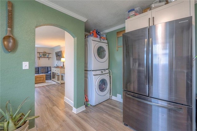 kitchen with arched walkways, stacked washer / dryer, light wood-style flooring, ornamental molding, and freestanding refrigerator