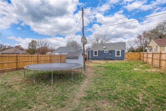 view of yard with a storage shed, a fenced backyard, a trampoline, and an outdoor structure