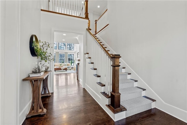 stairway featuring recessed lighting, baseboards, a high ceiling, and wood finished floors