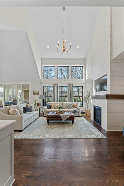 living room with a notable chandelier, high vaulted ceiling, recessed lighting, a fireplace, and dark wood-style flooring