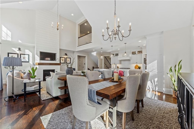 dining area with dark wood-type flooring, stairway, a notable chandelier, and a large fireplace