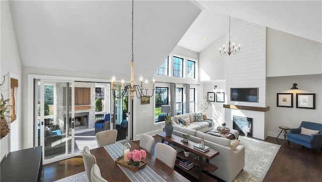 living area with baseboards, a fireplace, wood finished floors, a notable chandelier, and high vaulted ceiling