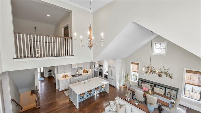 living area with high vaulted ceiling, crown molding, baseboards, a chandelier, and dark wood-style flooring