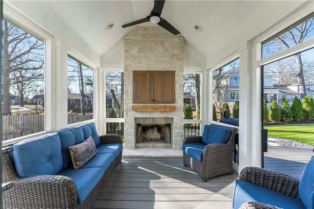 sunroom featuring a ceiling fan, vaulted ceiling, a healthy amount of sunlight, and an outdoor stone fireplace