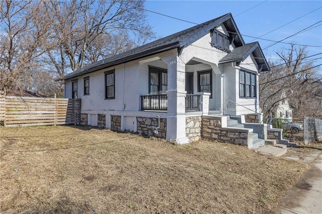 view of side of home with a porch, a shingled roof, fence, a lawn, and stucco siding