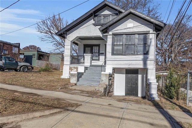 bungalow-style house with covered porch, fence, and stucco siding