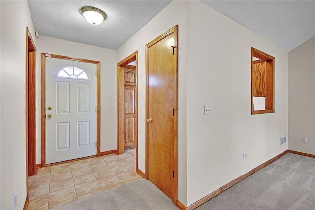 foyer entrance with light carpet, visible vents, a textured ceiling, and baseboards