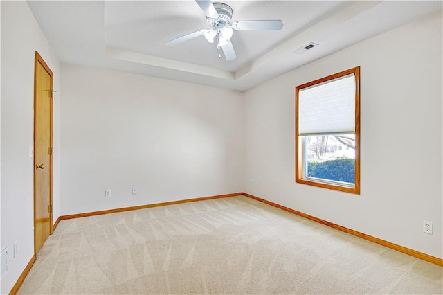 spare room featuring visible vents, baseboards, ceiling fan, a raised ceiling, and light colored carpet