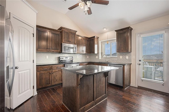 kitchen with a breakfast bar, a sink, vaulted ceiling, appliances with stainless steel finishes, and dark wood finished floors