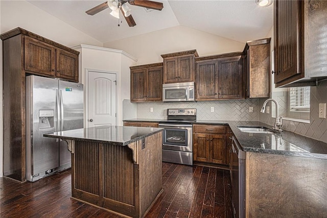 kitchen with appliances with stainless steel finishes, lofted ceiling, dark stone counters, and a sink