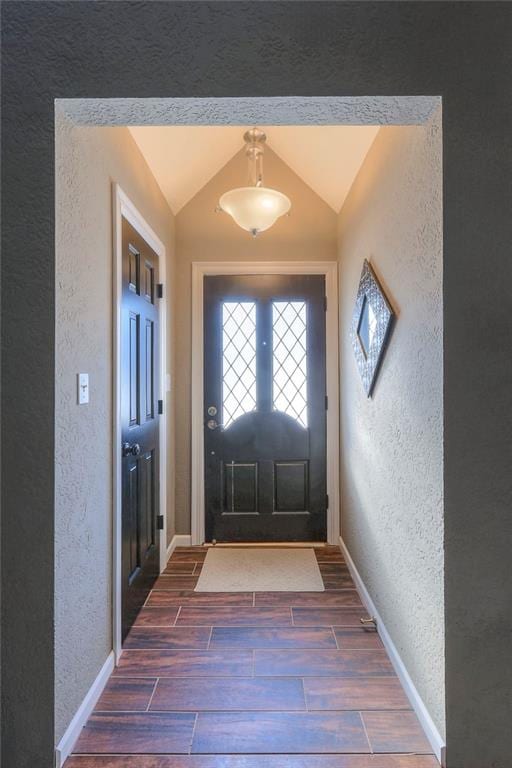 doorway to outside featuring wood finish floors, vaulted ceiling, a textured wall, and baseboards