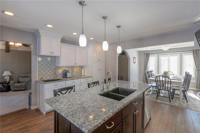 kitchen with arched walkways, backsplash, a sink, and dark wood finished floors