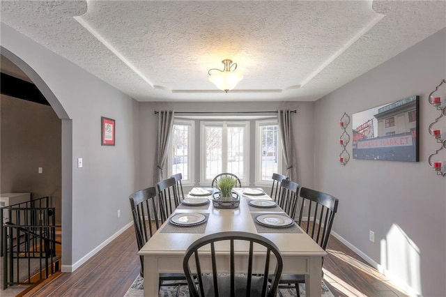 dining room with baseboards, a textured ceiling, arched walkways, and wood finished floors