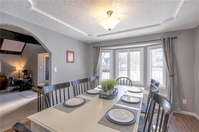 dining room featuring baseboards, arched walkways, a raised ceiling, and a textured ceiling