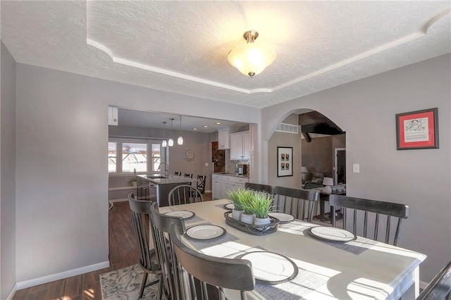 dining room featuring baseboards, a textured ceiling, arched walkways, and dark wood-style flooring