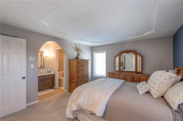 bedroom with a textured ceiling, arched walkways, connected bathroom, light carpet, and baseboards