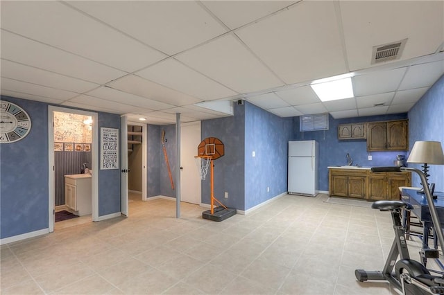 kitchen featuring baseboards, visible vents, a drop ceiling, freestanding refrigerator, and a sink