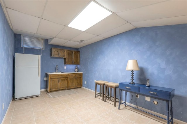 kitchen with freestanding refrigerator, a paneled ceiling, a sink, and light tile patterned floors