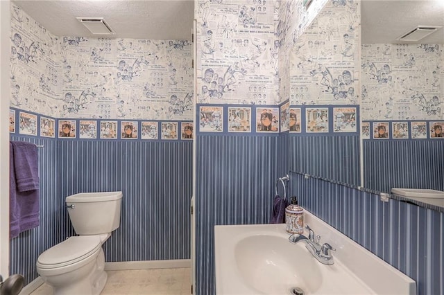 bathroom featuring toilet, a textured ceiling, visible vents, and a sink