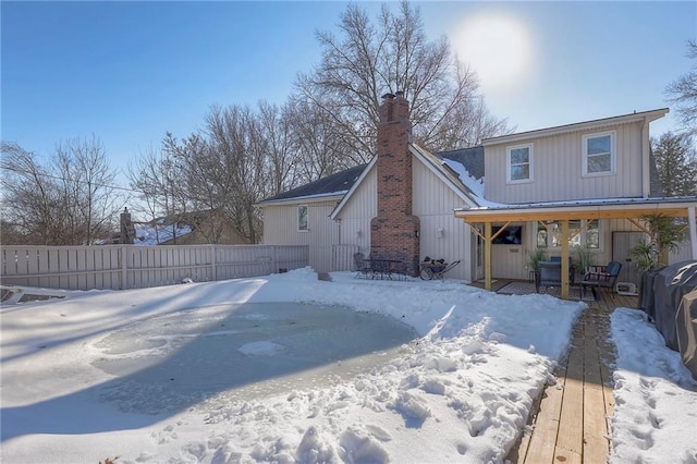 snow covered rear of property featuring fence and a chimney