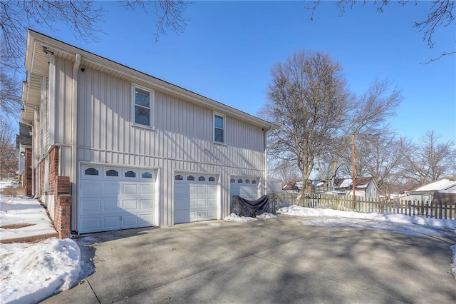 snow covered property with a garage, fence, and concrete driveway