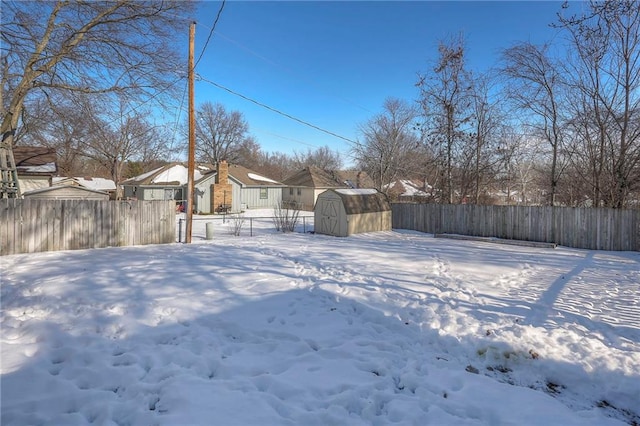 snowy yard featuring a fenced backyard, an outdoor structure, and a storage unit