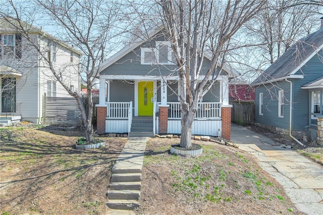 bungalow with brick siding, covered porch, and fence