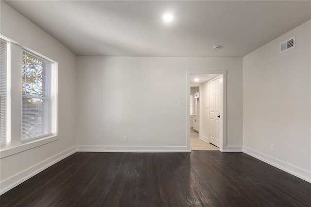 unfurnished room with dark wood-style flooring, visible vents, and baseboards