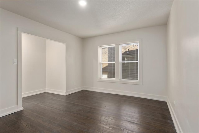 empty room featuring a textured ceiling, dark wood-type flooring, and baseboards