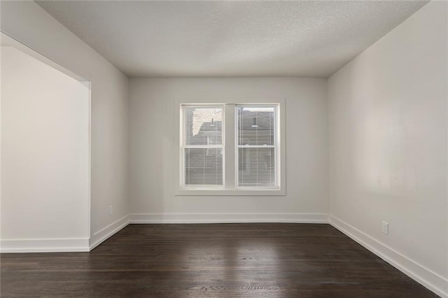 spare room with a textured ceiling, dark wood-style flooring, and baseboards