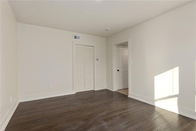 unfurnished room featuring visible vents, dark wood finished floors, and baseboards