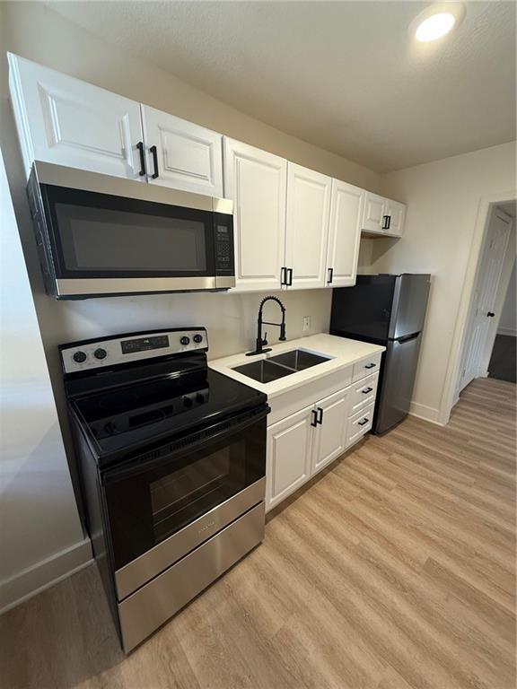 kitchen with appliances with stainless steel finishes, light wood-style floors, white cabinetry, and a sink