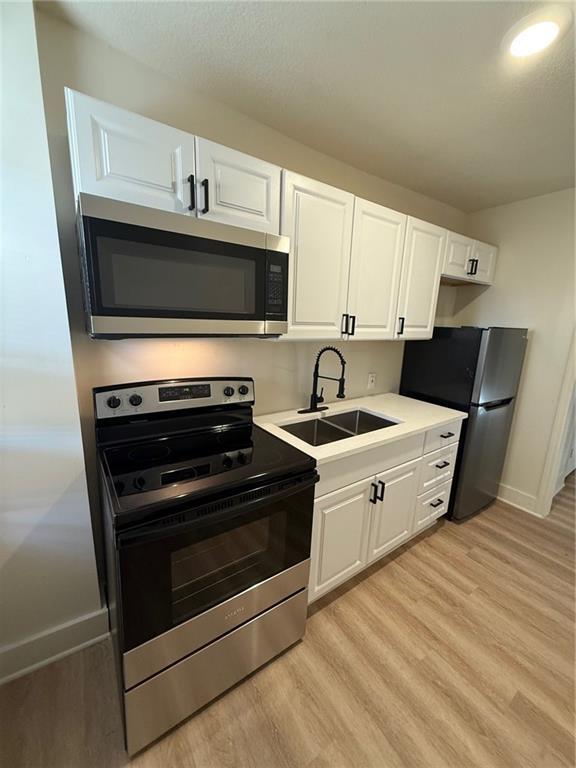 kitchen with light wood-type flooring, white cabinetry, stainless steel appliances, and a sink